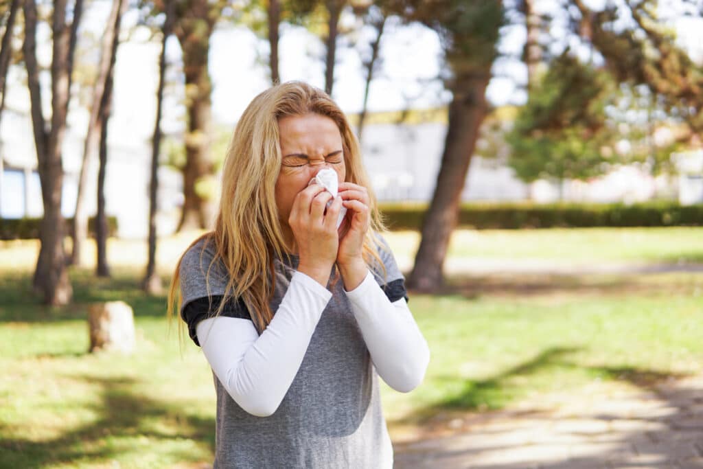 Woman suffering from spring allergy, blowing nose with a tissue in the park